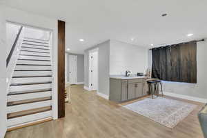 Bar area featuring gray cabinetry, light wood-type flooring, light stone countertops, and recessed lighting
