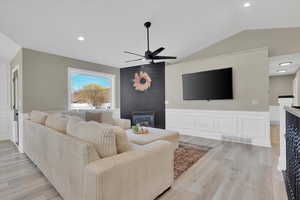 Living area featuring a wainscoted wall, a decorative wall, light wood-style floors, a ceiling fan, and lofted ceiling