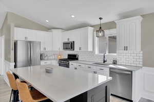 Dual tone kitchen with wainscoting, stainless steel appliances, a center island, decorative light fixtures, and a breakfast bar area