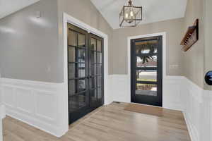 Entryway featuring wainscoting, a decorative wall, light wood-style floors, french doors, and suspended lighting