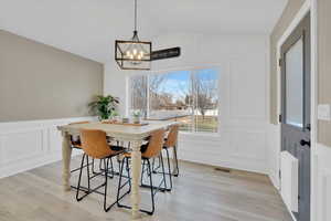 Dining room with a decorative wall, vaulted ceiling, light wood finished floors, a chandelier, and wainscoting