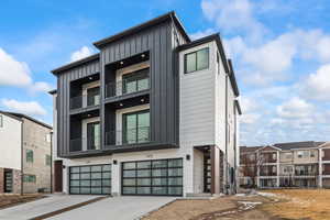 Modern home with board and batten siding, an attached garage, driveway, and a balcony