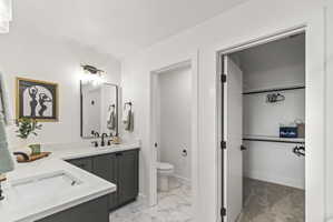 Full bath with double vanity, a spacious closet, and light marble finish flooring