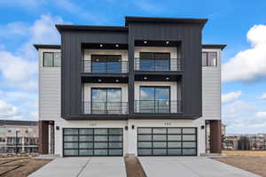 Contemporary house with an attached garage, concrete driveway, a balcony, and board and batten siding