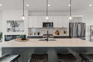 Kitchen featuring a breakfast bar area, two tone cabinetry, stainless steel appliances, hanging light fixtures, and light stone countertops