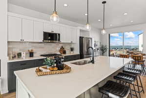 Kitchen with two tone cabinetry, stainless steel appliances, decorative light fixtures, a center island with sink, and a breakfast bar
