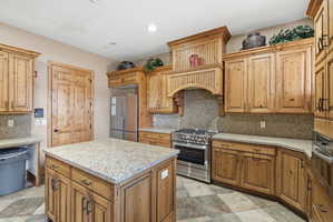 Kitchen with decorative backsplash, stainless steel appliances, light stone countertops, a center island, and recessed lighting