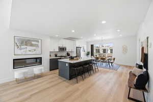 Kitchen featuring dual tone cabinets, a breakfast bar area, a center island with sink, light wood-style floors, and stainless steel appliances