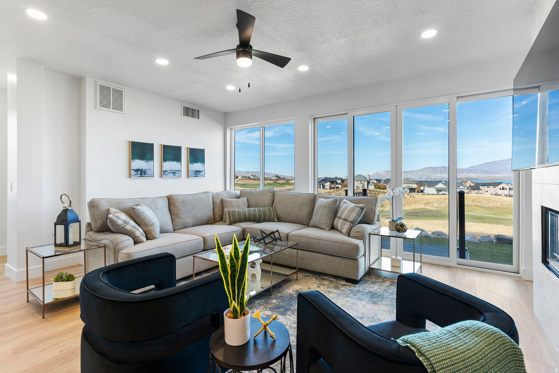 Spacious living area featuring expansive glass sliding doors, recessed lighting, a modern ceiling fan, wood-finish flooring, and a built-in fireplace with a tiled surround