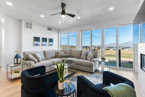 Spacious living area featuring expansive glass sliding doors, recessed lighting, a modern ceiling fan, wood-finish flooring, and a built-in fireplace with a tiled surround