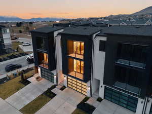 Exterior entry at dusk featuring an attached garage, concrete driveway, and roof with shingles
