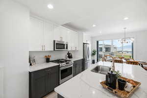 Kitchen with stainless steel appliances, dual tone cabinetry, light stone countertops, a chandelier, and decorative backsplash