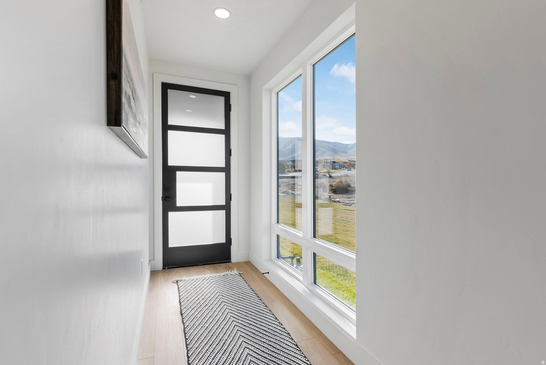 Entryway featuring a contemporary black door with frosted glass panels, wood-finish flooring, recessed lighting, and a large multi-pane window
