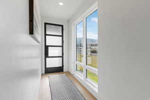 Entryway featuring a contemporary black door with frosted glass panels, wood-finish flooring, recessed lighting, and a large multi-pane window