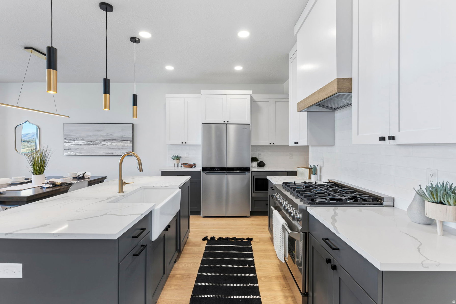 Kitchen featuring a large island with a farmhouse sink, stainless steel appliances, two-tone cabinetry, wood-finish flooring, and pendant lighting