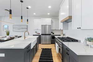 Kitchen featuring a large island with a farmhouse sink, stainless steel appliances, two-tone cabinetry, wood-finish flooring, and pendant lighting