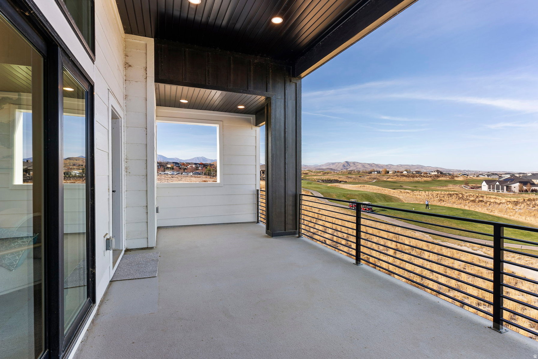 Expansive outdoor balcony featuring concrete flooring, black horizontal bar railing, and a tongue and groove soffit ceiling with recessed lighting