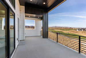 Expansive outdoor balcony featuring concrete flooring, black horizontal bar railing, and a tongue and groove soffit ceiling with recessed lighting