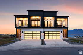 Modern duplex exterior featuring a dark upper facade with multiple balconies, white lower level, and two translucent panel garage doors