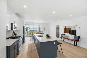 Two tone kitchen featuring stainless steel appliances, light stone counters, light wood-style flooring, a mountain view, and a breakfast bar