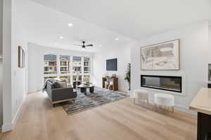 Living room with a glass covered fireplace, light wood-style flooring, a ceiling fan, and recessed lighting