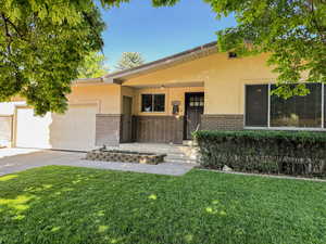 View of front of property featuring brick siding, stucco siding, an attached garage, a front yard, and a porch