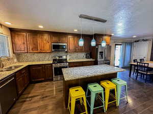 Kitchen featuring stainless steel appliances, a breakfast bar, a kitchen island, light stone counters, and a textured ceiling