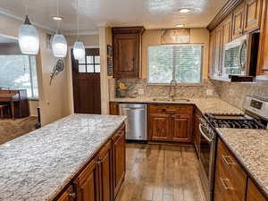 Kitchen with stainless steel appliances, dark wood finished floors, decorative backsplash, decorative light fixtures, and wood finish cabinetry