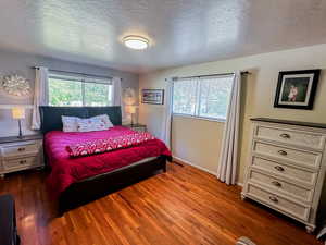 Bedroom with a textured ceiling, dark wood-style flooring, and multiple windows