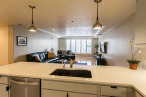 Kitchen with open floor plan, a raised ceiling, dishwasher, pendant lighting, and light stone counters