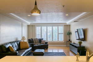 Living area featuring a raised ceiling, a textured ceiling, light wood-style flooring, crown molding, and recessed lighting