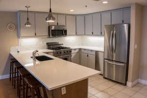 Kitchen featuring stainless steel appliances, a peninsula, a kitchen bar, decorative light fixtures, and tasteful backsplash