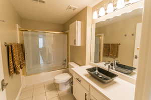Full bathroom with vanity, a textured ceiling, light tile patterned floors, and shower / bath combination with glass door