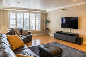 Living area featuring wood finished floors, ornamental molding, a tray ceiling, and a textured ceiling