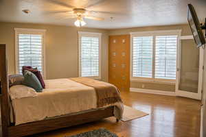 Bedroom with multiple windows, a textured ceiling, hardwood / wood-style flooring, and ceiling fan