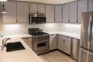 Kitchen featuring stainless steel appliances, gray cabinetry, decorative backsplash, and light tile patterned flooring