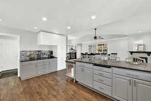 Kitchen with white cabinetry, dark stone counters, dark wood-style flooring, ceiling fan, and backsplash