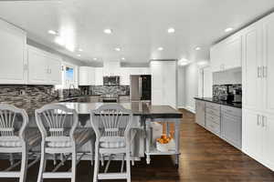 Kitchen with decorative backsplash, a breakfast bar area, white cabinetry, stainless steel appliances, and dark wood-type flooring