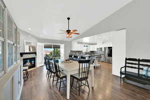 Dining room with a glass covered fireplace, ceiling fan, dark wood-style flooring, vaulted ceiling, and recessed lighting