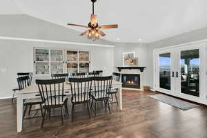 Dining area featuring dark wood finished floors, a glass covered fireplace, vaulted ceiling, and ceiling fan