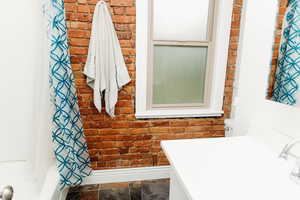 Full bathroom featuring brick wall, vanity, shower / bath combo with shower curtain, and dark stone finish floors