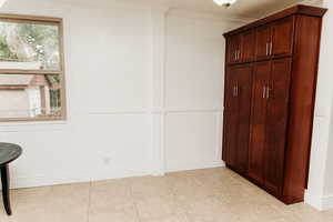 Dining area with wainscoting, multiple windows, ornamental molding, cabinetry/pantry and light tile patterned floors