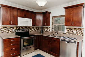 Kitchen with stainless steel appliances, light tile patterned flooring, light granite countertops, backsplash, and crown molding