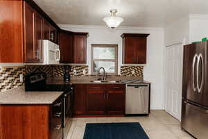 Kitchen featuring stainless steel appliances, light granite countertops, crown molding, decorative backsplash, and light tile patterned floors