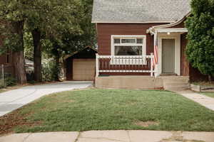 View of front of property with roof with shingles, a front lawn and detached garage