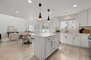 Kitchen featuring subway tile backsplash, open concept floor plan, white cabinetry, quartz counters and stainless steel appliances.