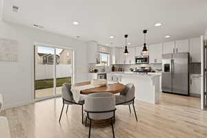 Semi-formal dining space featuring light LVP flooring and access to backyard through the sliding glass door. The dining area is open to the spacious kitchen.