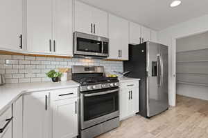 Kitchen featuring subway tile backsplash, open concept floor plan, white cabinetry, quartz counters and stainless steel appliances.