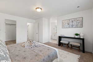 Primary bedroom featuring carpet flooring, light paint, ensuite bathroom, and walk-in closet