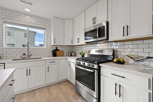 Kitchen featuring subway tile backsplash, open concept floor plan, white cabinetry, quartz counters and stainless steel appliances.